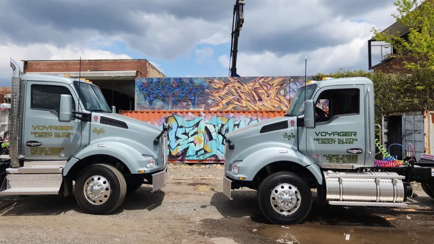 Two Voyager Kenworth daycabs in front of a graffiti wall in the Newark yard